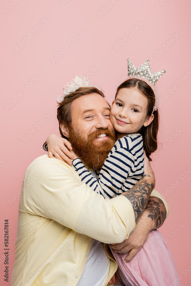 Cheerful father and daughter in crowns hugging isolated on pink. Cheerful father and daughter in crowns hugging isolated on pink.