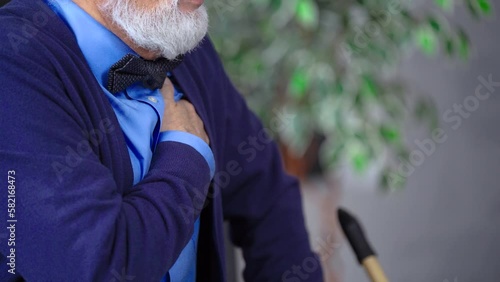Grandfather, an elderly senior man, sits, clutches his chest, has a heartache, breathes heavily, sighs, close-up
