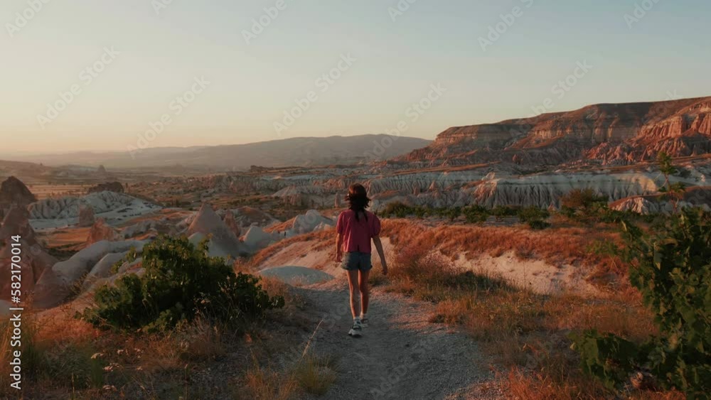 Camera follows happy teen age girl walking down beautiful rock cliffs on vacation in summer sunset Cappadocia background Camera follows happy teen age girl walking down beautiful rock cliffs on vacation in summer sunset Cappadocia background
