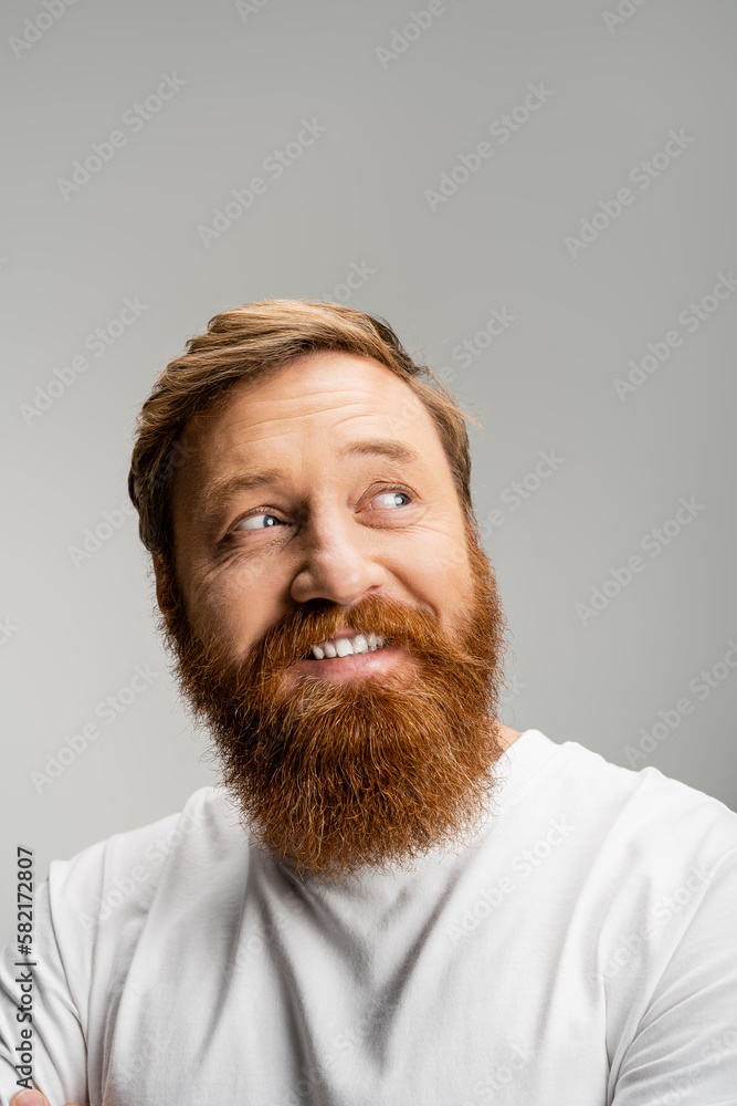 Carefree bearded man in white t-shirt looking away isolated on grey. Carefree bearded man in white t-shirt looking away isolated on grey.