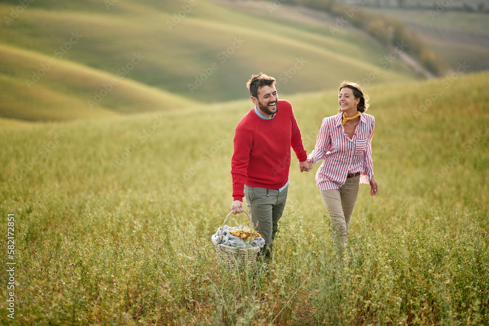 A young cheerful couple is excited about a picnic they will have on a large meadow. Love, relationship, together, nature A young cheerful couple is excited about a picnic they will have on a large meadow. Love, relationship, together, nature