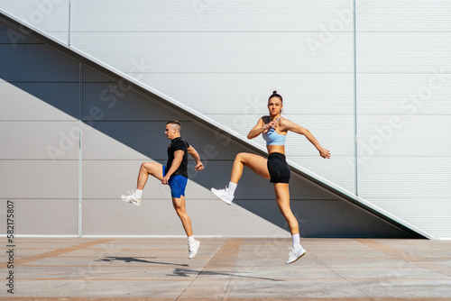 Fit couple moving and jumping. They are stretching and warming up their bodies before training, on a beautiful sunny day