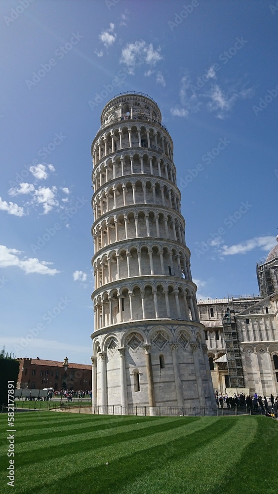 Pisa, Italy - Apr 08 2018: Exterior of the Torre di Pisa, Leaning Tower of Pisa, with Cattedrale di Pisa in the background with a bright blue sky and clouds in spring