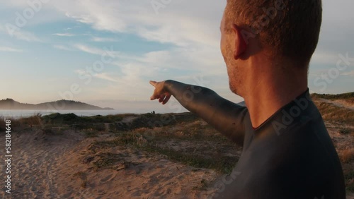 Surfer in wetsuit points to the spot on the horizon photo