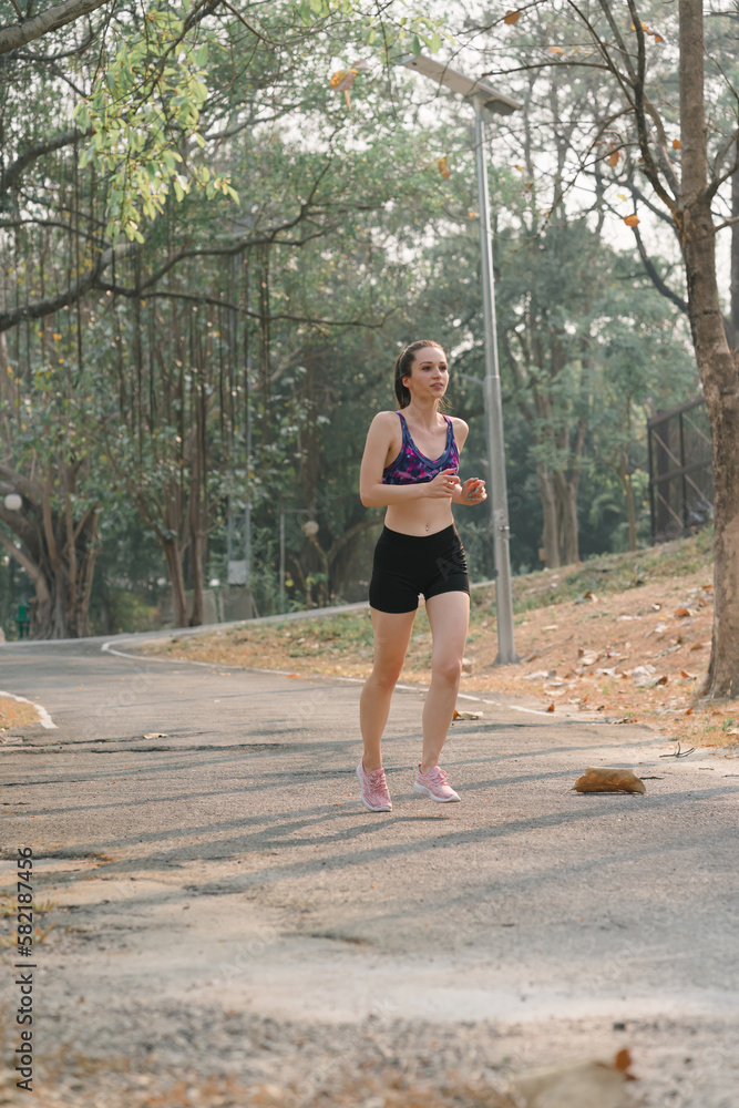 A beautiful sportswoman in sportswear is jogging outdoors in Autumn city park background.