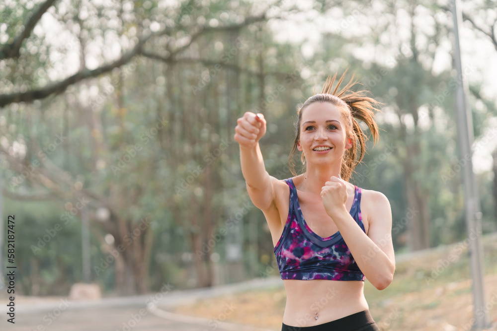 A beautiful sportswoman in sportswear is performing boxing exercises outdoors in an Autumn city park background. A beautiful sportswoman in sportswear is performing boxing exercises outdoors in an Autumn city park background.