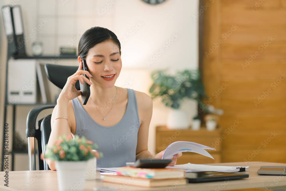 A beautiful young businesswoman is shown working on a laptop computer in her home office. The image represents the concept of working from home.