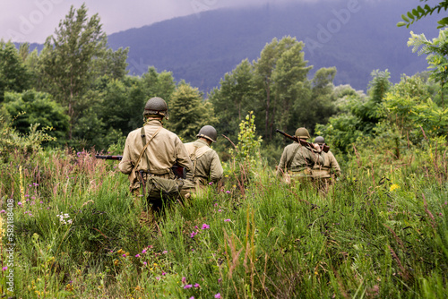 Historical reconstruction. World War II infantry division soldiers patrol a site in the tall grass. View from the back.  Porąbka, Poland photo