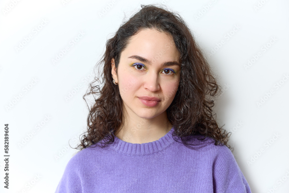 Closeup portrait of caucasian woman with dark curly hair wearing creative makeup purple eye shadow and purple sweater. She is looking at camera and smiling happily against white background. Closeup portrait of caucasian woman with dark curly hair wearing creative makeup purple eye shadow and purple sweater. She is looking at camera and smiling happily against white background.