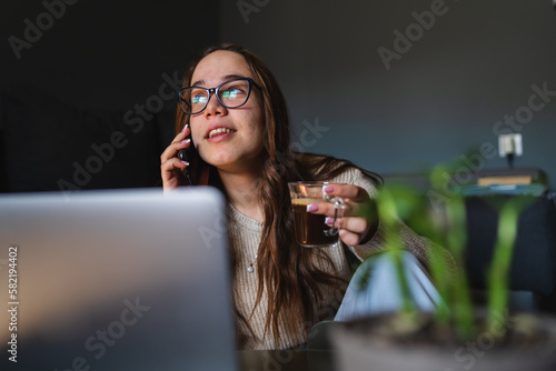 A young girl sitting at home while using laptop to study or do business while drinking coffee and using mobile phone