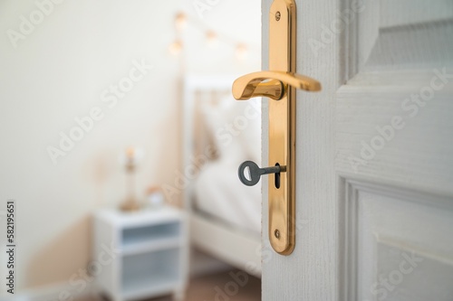 Closeup shot of a white open door with a key in it with a bedroom in a blurry background.