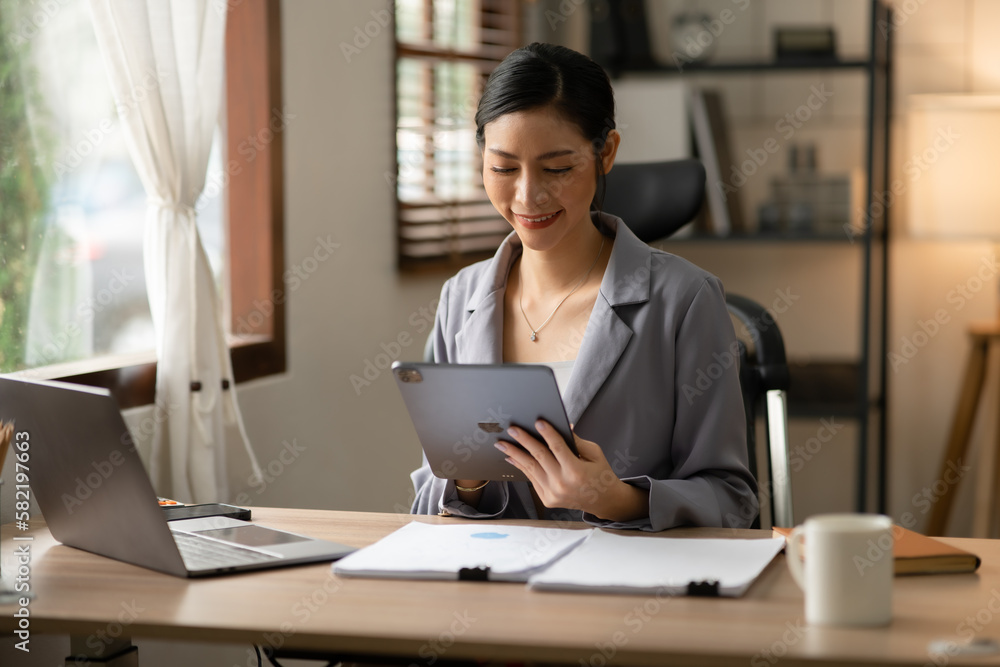 Young Asian businesswoman reading graphs and talking on phone with customers in office Young Asian businesswoman reading graphs and talking on phone with customers in office