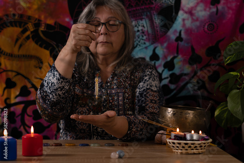 Elderly white-haired woman holding a pendulum in a divination session with candles and incense
