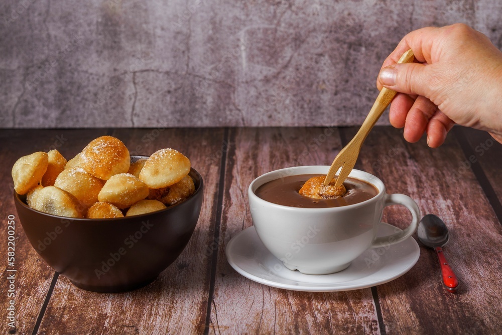 woman spreading a sugared fritter with a wooden fork on a hot chocolate woman spreading a sugared fritter with a wooden fork on a hot chocolate