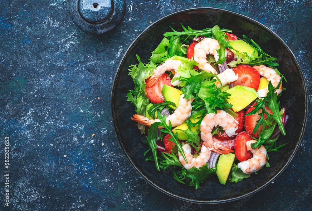 Strawberry, shrimp and herbs healthy salad with arugula, avocado and onion, blue kitchen table. Fresh useful dish for healthy eating