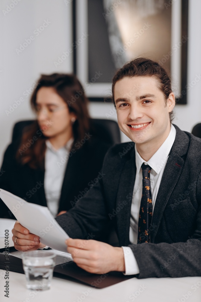 Smiling young businessman holding document. Indoor shot of happy manager doing paperwork in office. Man posing during business conference Smiling young businessman holding document. Indoor shot of happy manager doing paperwork in office. Man posing during business conference