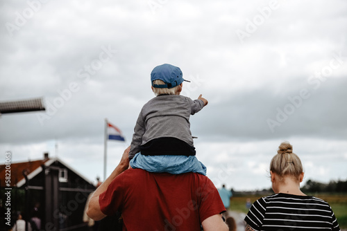 Un niño pequeño señala al frente mientras es llevado a hombros por su padre. Concepto de viajar con hijos.