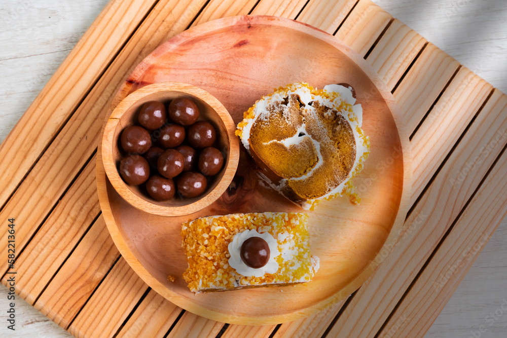 Slices of mocha flavored bread rolls covered with milk cream and nuts topped with chocolate balls on a wooden plate Slices of mocha flavored bread rolls covered with milk cream and nuts topped with chocolate balls on a wooden plate