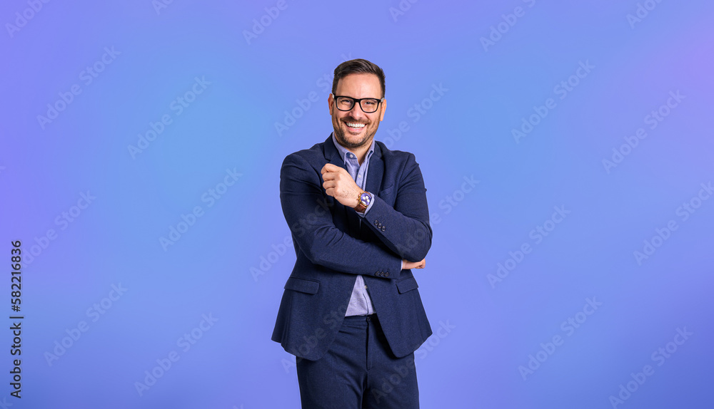 Portrait of confident young adult handsome CEO dressed in blue suit wearing eyeglasses and posing cheerfully against blue background Portrait of confident young adult handsome CEO dressed in blue suit wearing eyeglasses and posing cheerfully against blue background