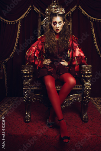 Woman dressed as the queen of hearts, creative make up with big heart on eye, girl sitting in the throne, hi-end retouched portrait photo