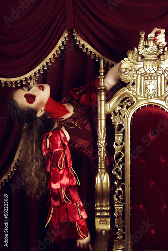 Woman dressed as the queen of hearts, creative make up with big heart on eye, girl sitting in the throne, hi-end retouched portrait