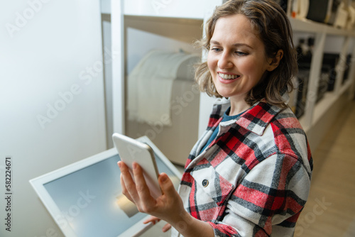 A woman stands next to self service kiosk in a store and looks into a smartphone