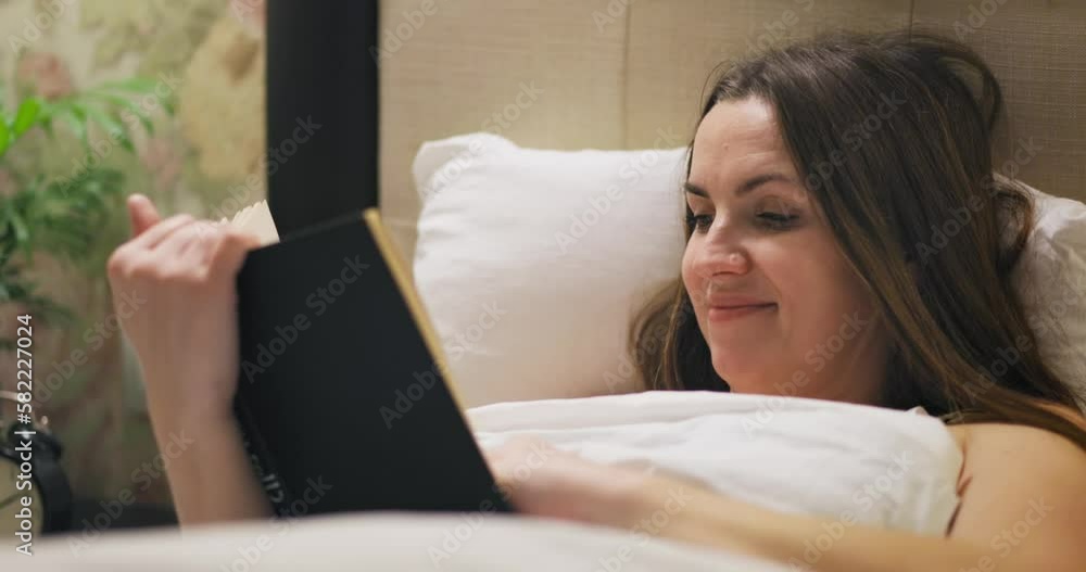 Young woman is reading interesting book while lying in bed Young woman is reading interesting book while lying in bed