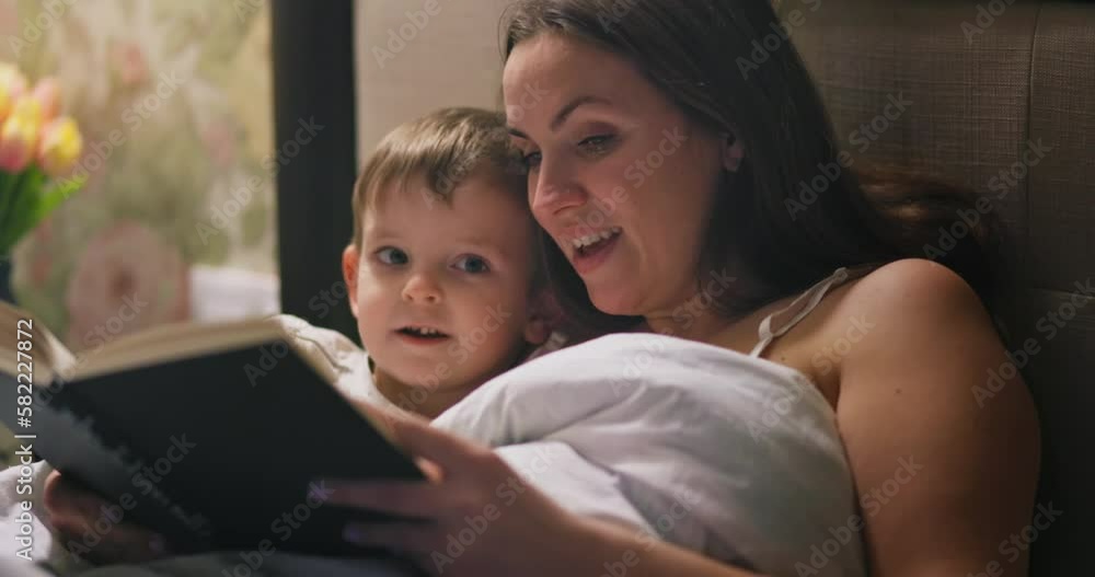 Mother reading a fairytale to her lovely small son in bed before going to sleep Mother reading a fairytale to her lovely small son in bed before going to sleep