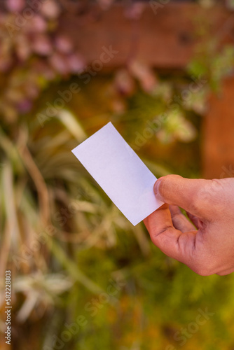 papel rectangular blanco vale sostenido por mano sosteniendo papel ticket sobre fondo de plantas