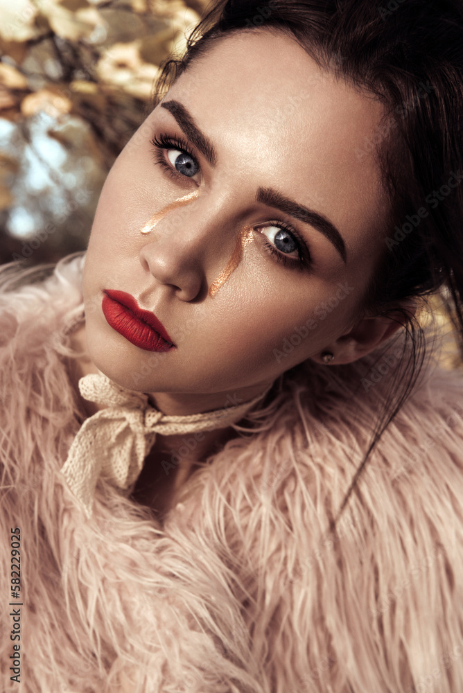 Fashion Female Model In Fashionable Clothes fur coat posing In autumn forest. Creative make up gold tears and red lips. Hi-end retouched portrait Fashion Female Model In Fashionable Clothes fur coat posing In autumn forest. Creative make up gold tears and red lips. Hi-end retouched portrait