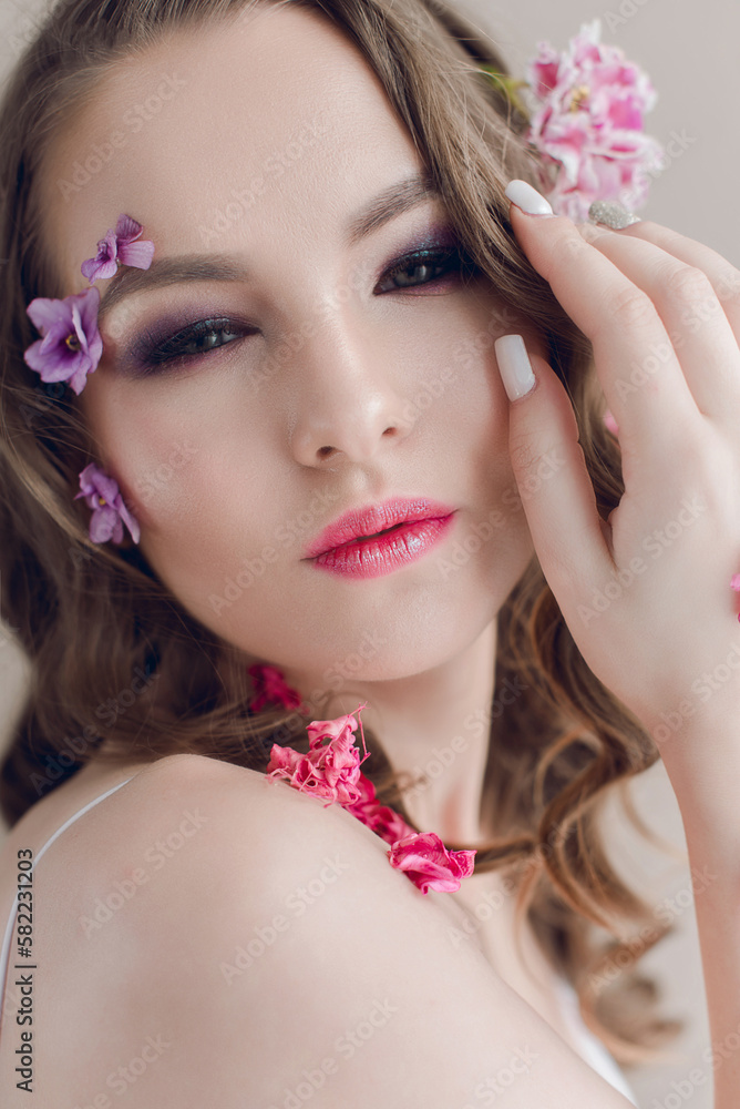Cosmetics and manicure. Close-up portrait of attractive woman with dry flowers on her face and hair, pastel color, perfect make-up and skin on blue background. Fresh, trendy, spring retouched portrait Cosmetics and manicure. Close-up portrait of attractive woman with dry flowers on her face and hair, pastel color, perfect make-up and skin on blue background. Fresh, trendy, spring retouched portrait