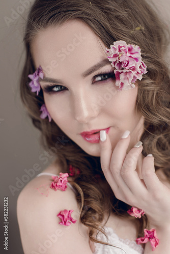 Cosmetics and manicure. Close-up portrait of attractive woman with dry flowers on her face and hair  pastel color  perfect make-up and skin on blue background. Fresh  trendy  spring retouched portrait