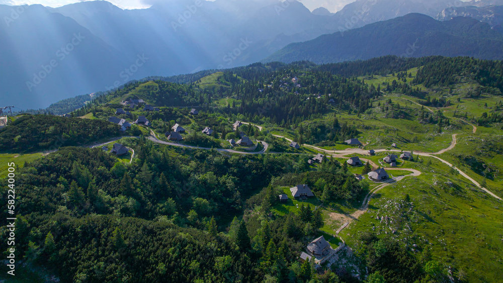 AERIAL: Fairy-tale wooden shepherd's huts among green forest trees and meadows