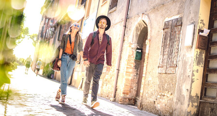 Happy couple in love having fun walking at old city center - Wanderlust life style and travel concept with young trendy tourists on sightseeing experience - Warm sunshine filter on tilted composition