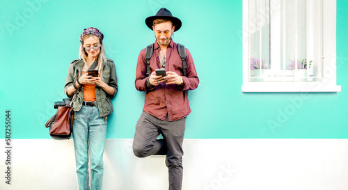 Young hipster couple having fun with mobile smart phone at out side location - Technology concept with connected friends sharing story content on social media networks - Bright teal and orange filter