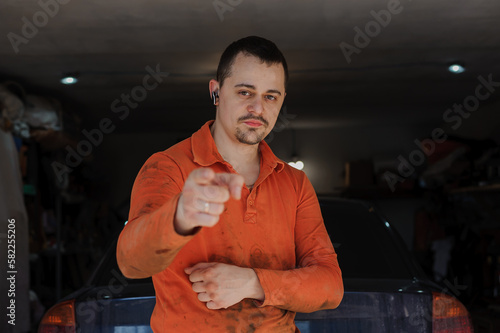 An auto mechanic stands near the garage in front of the car. A man stands near the garage in dirty work clothes