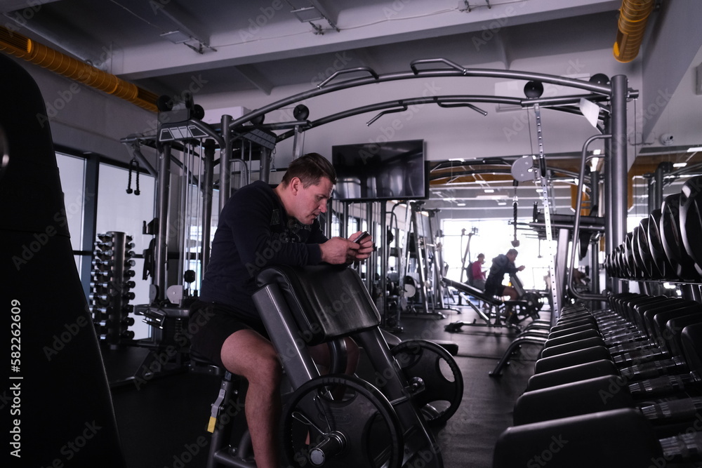 Fototapeta premium Sports equipment in the gym. Man in Stylish sports space. Expanders and simulators with heavy dumbbells. Bench press, anaerobic and aerobic exercises.