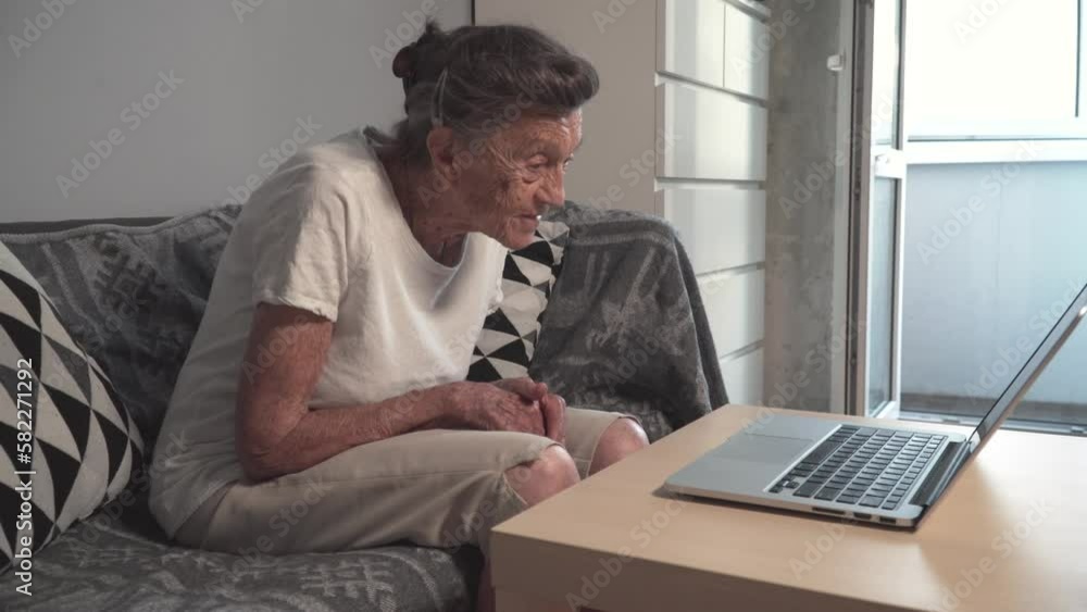 Senior woman using laptop at home. Elderly people learning modern technology. Smiling senior woman waving with hand while having video call on laptop. Senior lifestyle. Mature woman using internet. Senior woman using laptop at home. Elderly people learning modern technology. Smiling senior woman waving with hand while having video call on laptop. Senior lifestyle. Mature woman using internet.