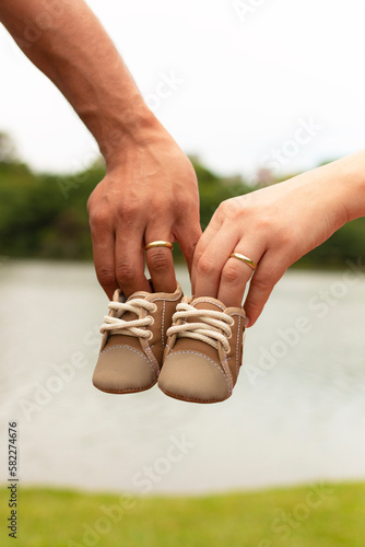 Mão de homem e mão de mulher usando aliança, segurando sapatinho de bebê. photo