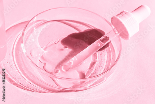 Petri dish. With transparent gel. With a pipette. Cosmetics bottle. On a pink background.