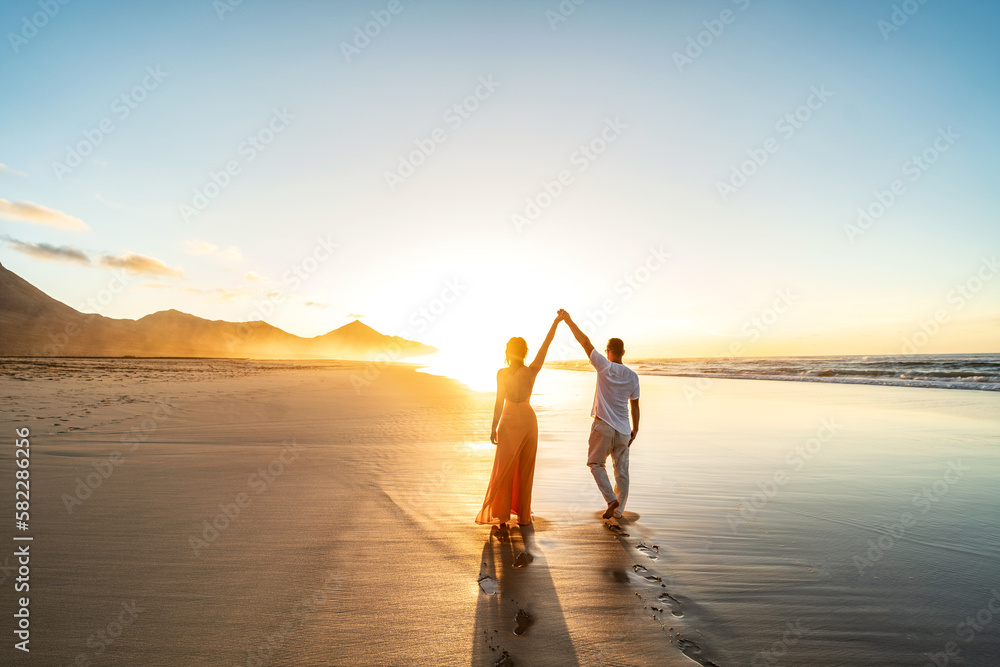 Lovely, romantic couple walking on sunset beach, enjoying evening light ...