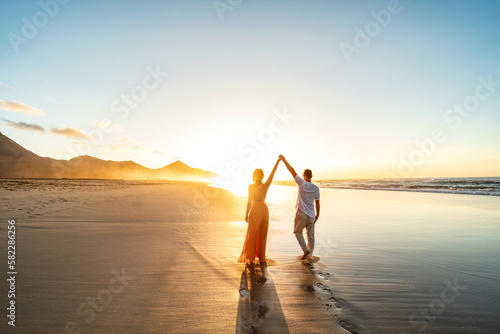 Lovely, romantic couple walking on sunset beach, enjoying evening light, relaxing on tropical summer vacation.