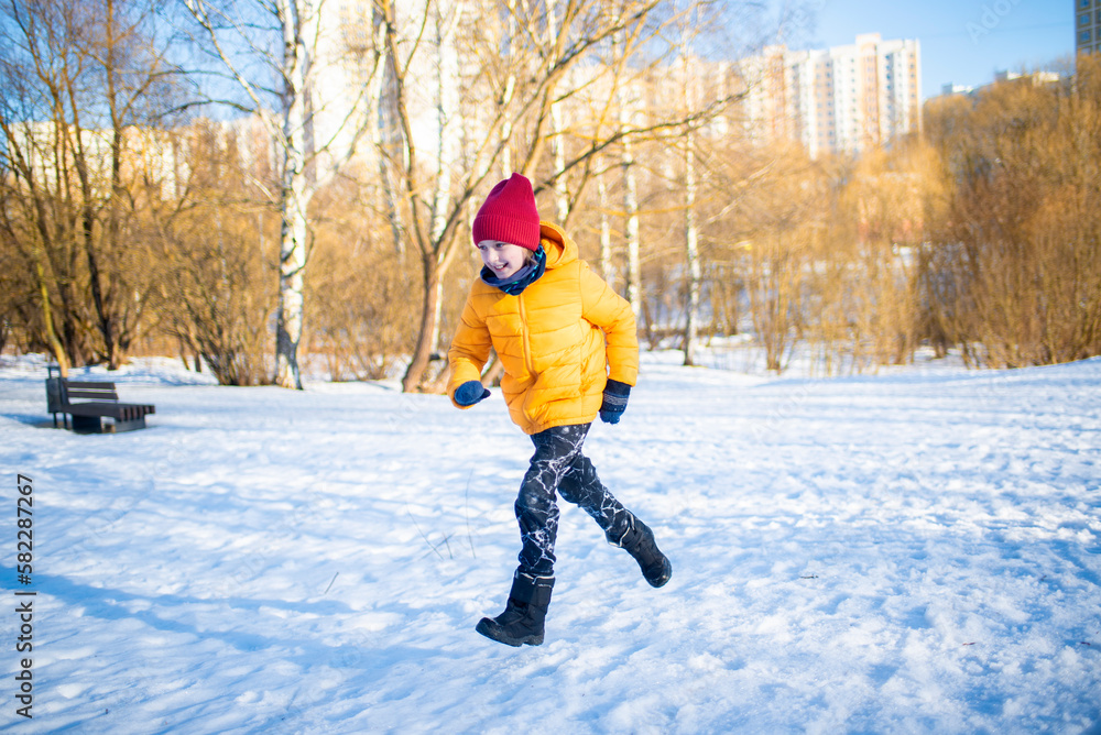 happy boy in colorful clothes runs through the snowy winter park