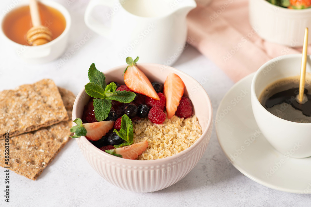 Oatmeal porridge with fruit and berries in bowl with spoon on white wooden background table top view, homemade healthy breakfast cereal with strawberry,