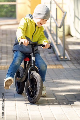 Little caucasian boy riding a balance bike in a play park. Kid learning biking. © Linas T
