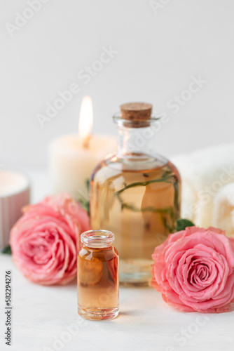 Aromatherapy. Concept of pure organic essential rose oil. Elixir with plant based floral or herbal ingredients. Pink flowers extract. Spa atmosphere with candle  towel. White background