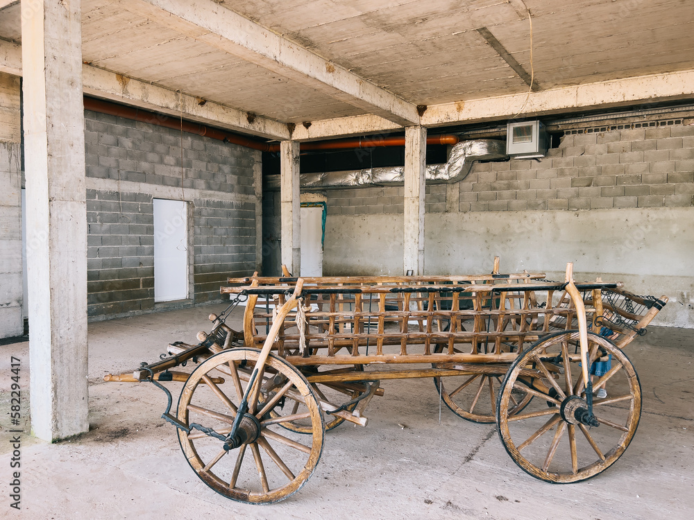Wooden cart on wheels stands under a concrete canopy in a parking lot