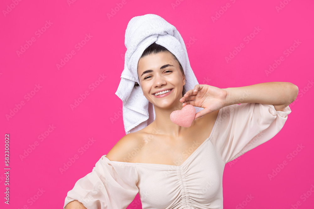 Beautiful cheerful attractive girl with a towel on her head, holds a sponge in the form of a pink heart. Beautiful cheerful attractive girl with a towel on her head, holds a sponge in the form of a pink heart.