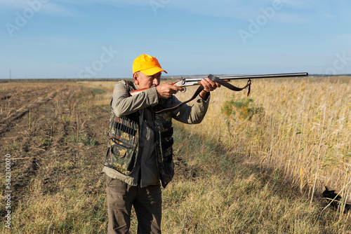 Hunter aiming with rifle while standing against sky