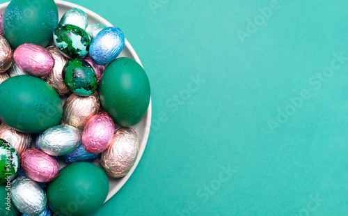 Mockup Easter food, treat. Colored chicken, quail eggs, chocolate eggs, sweets wrapped in bright foil on plate, top view. Flatly copy space, horizontal. Christian holiday tradition. Confectionary